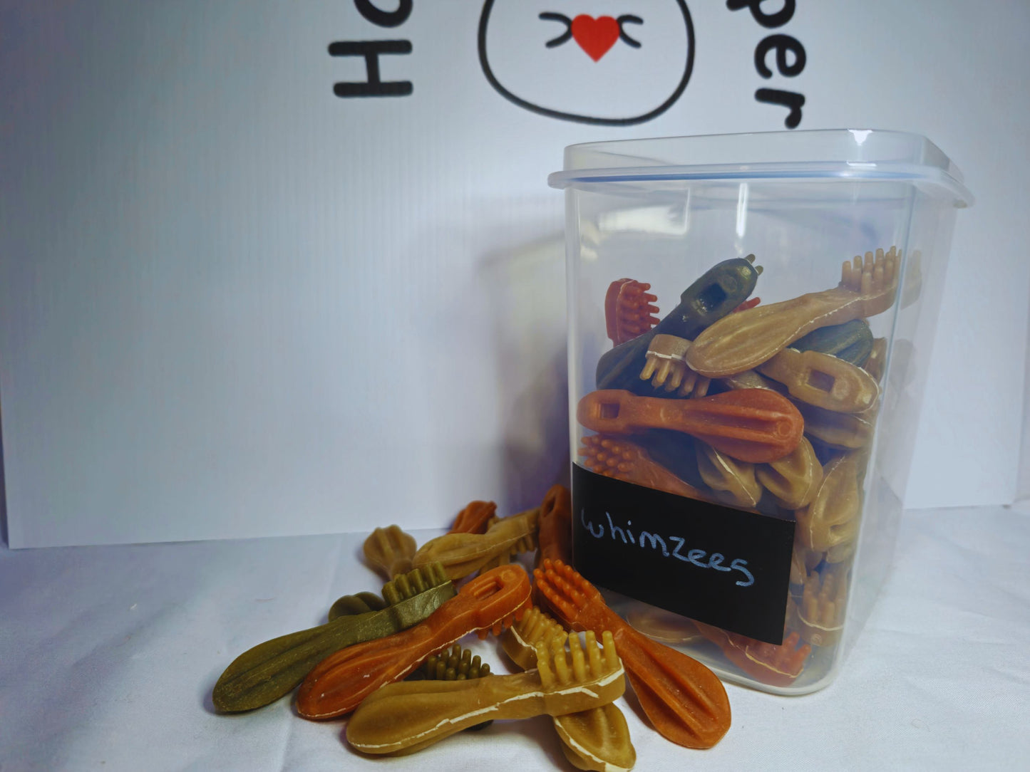 A plastic jar with a label that says Whimzees, the jar is full of hamster safe whimzees and there are some in front of the jar too.