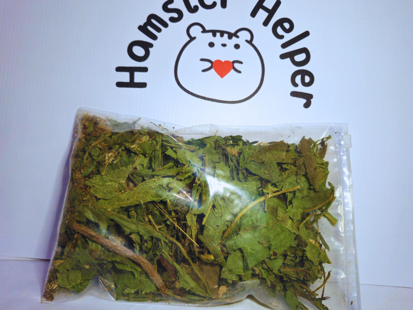 Dandelion forage in a bag in front of the Hamster Helper logo.