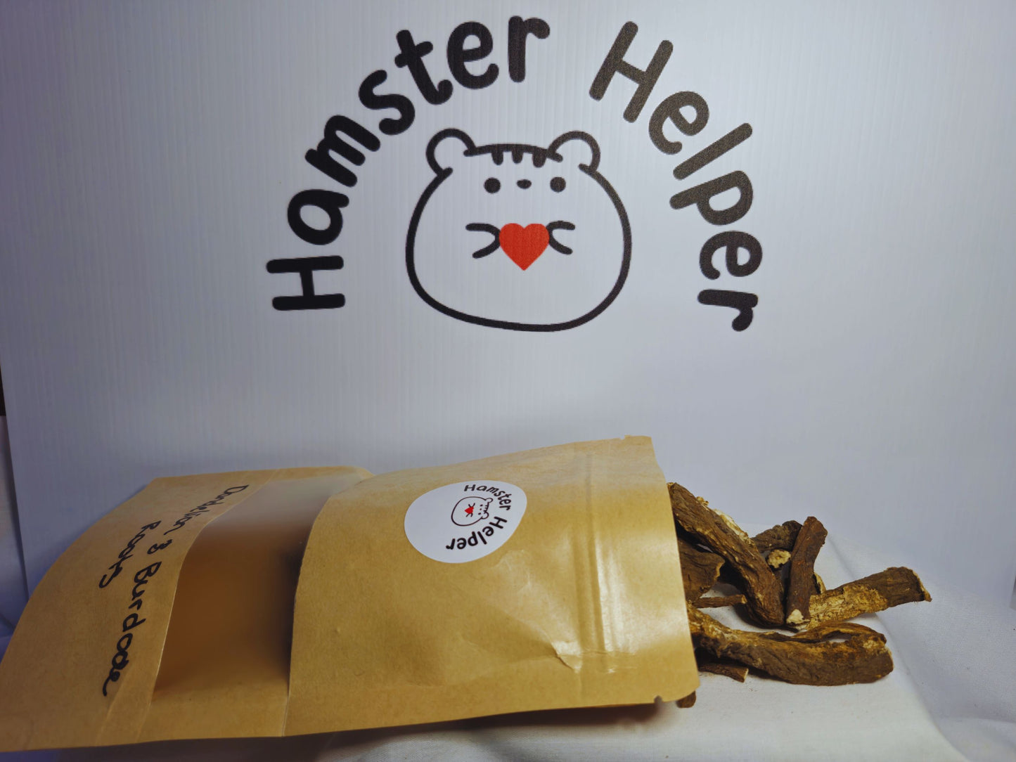 A close up of the mixed hamster safe dandelion and burdock roots spilling out of the pouch in front of the Hamster Helper logo.