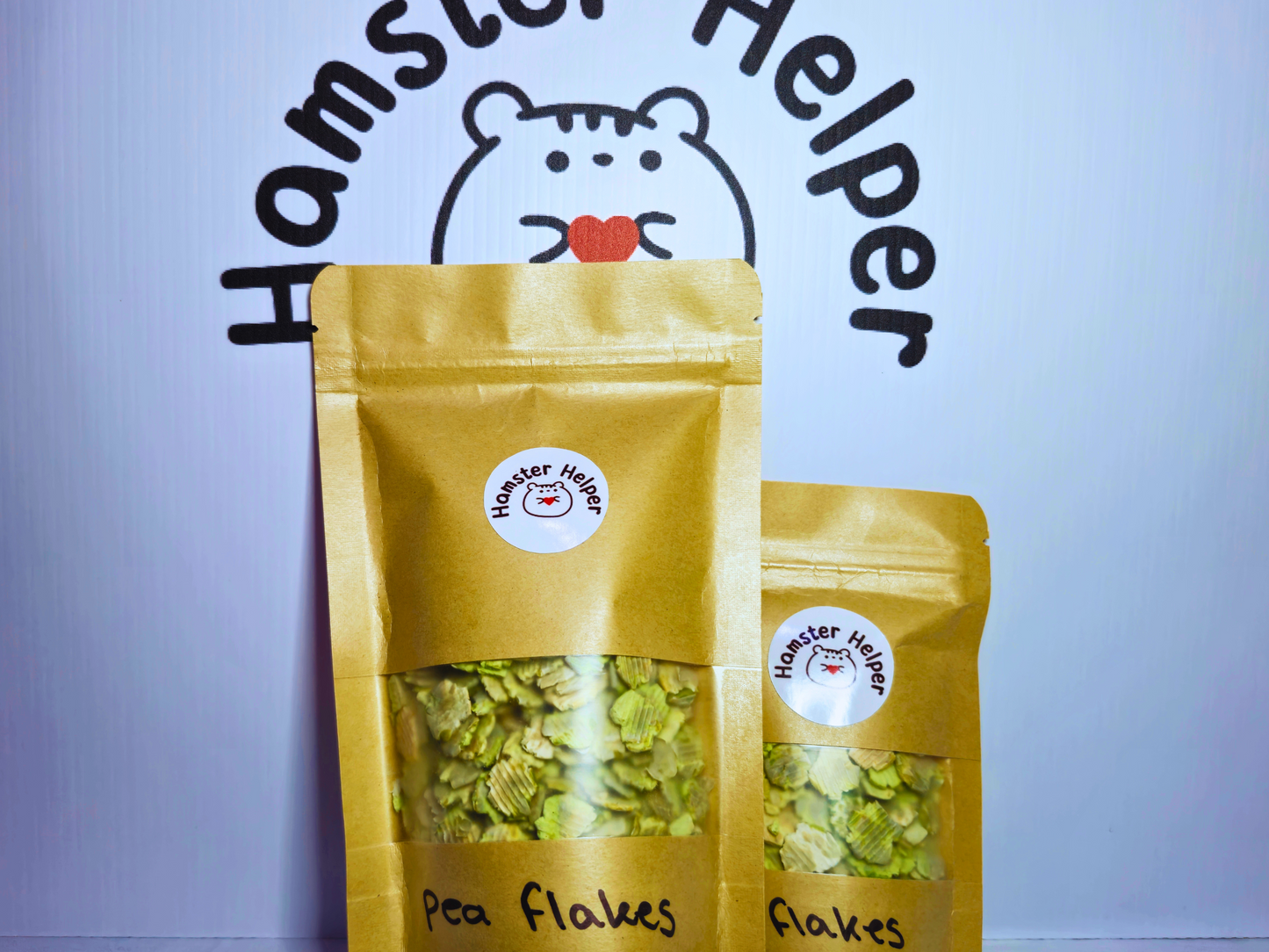 A large and small bag of hamster safe pea flakes in front of the hamster helper logo