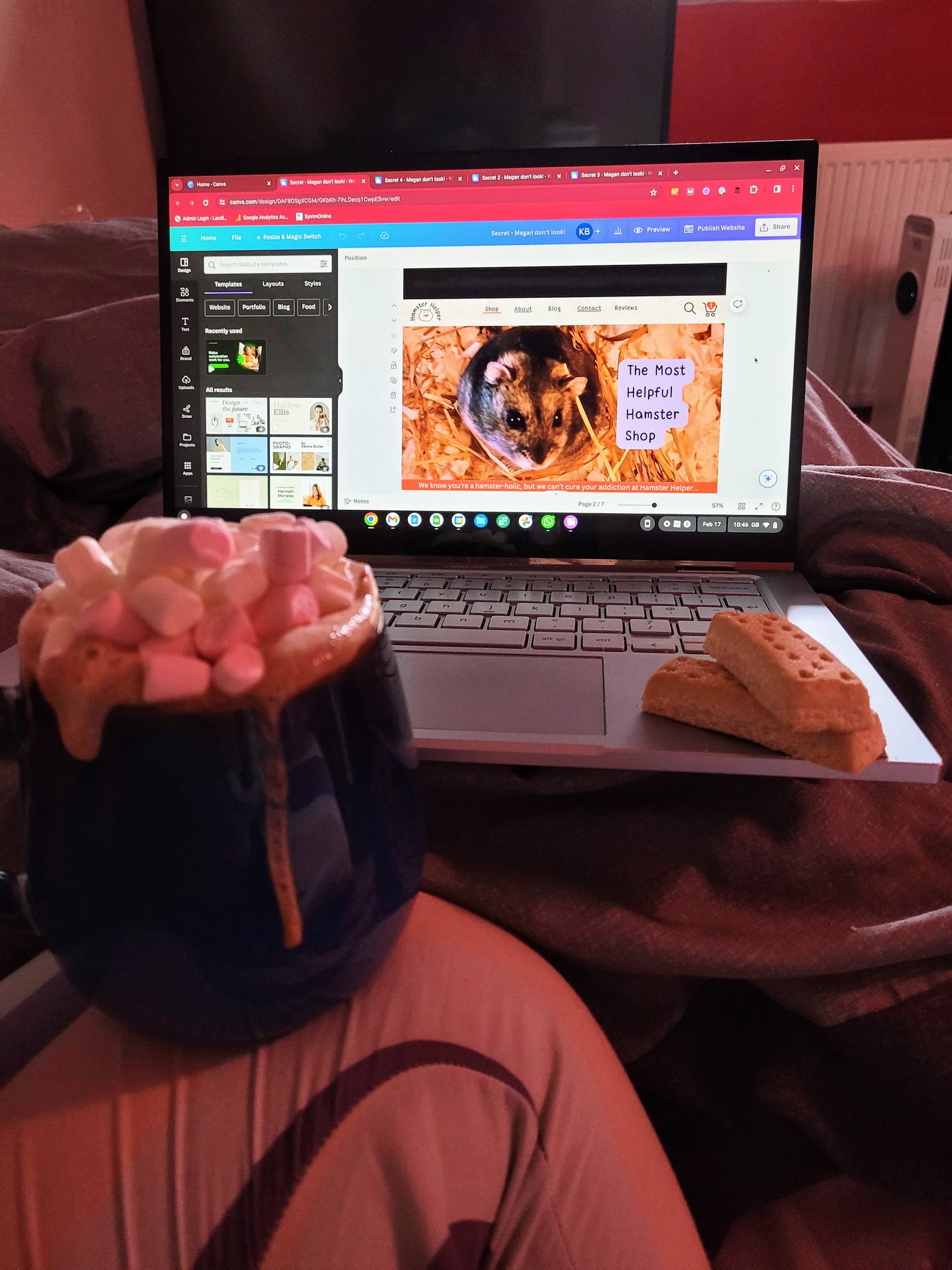 A laptop showing the Hamster Helper website being built, there are two shortbread fingers on the laptop and in the foreground there is a hot chocolate with whipped cream and marshmallows resting on a bent knee