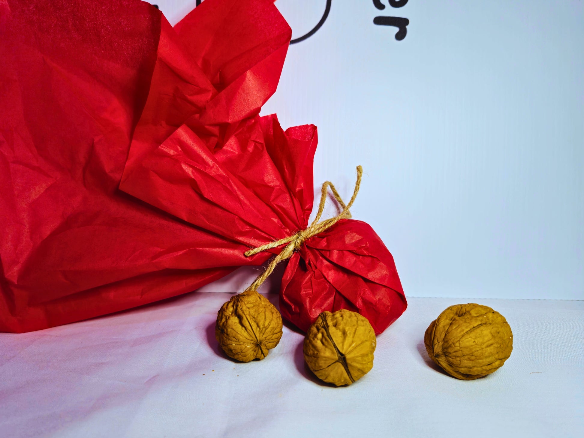 Walnuts wrapped in red paper and jute twine to demonstrate the packaging surrounded by three walnuts in shells for hamster tooth wearing.