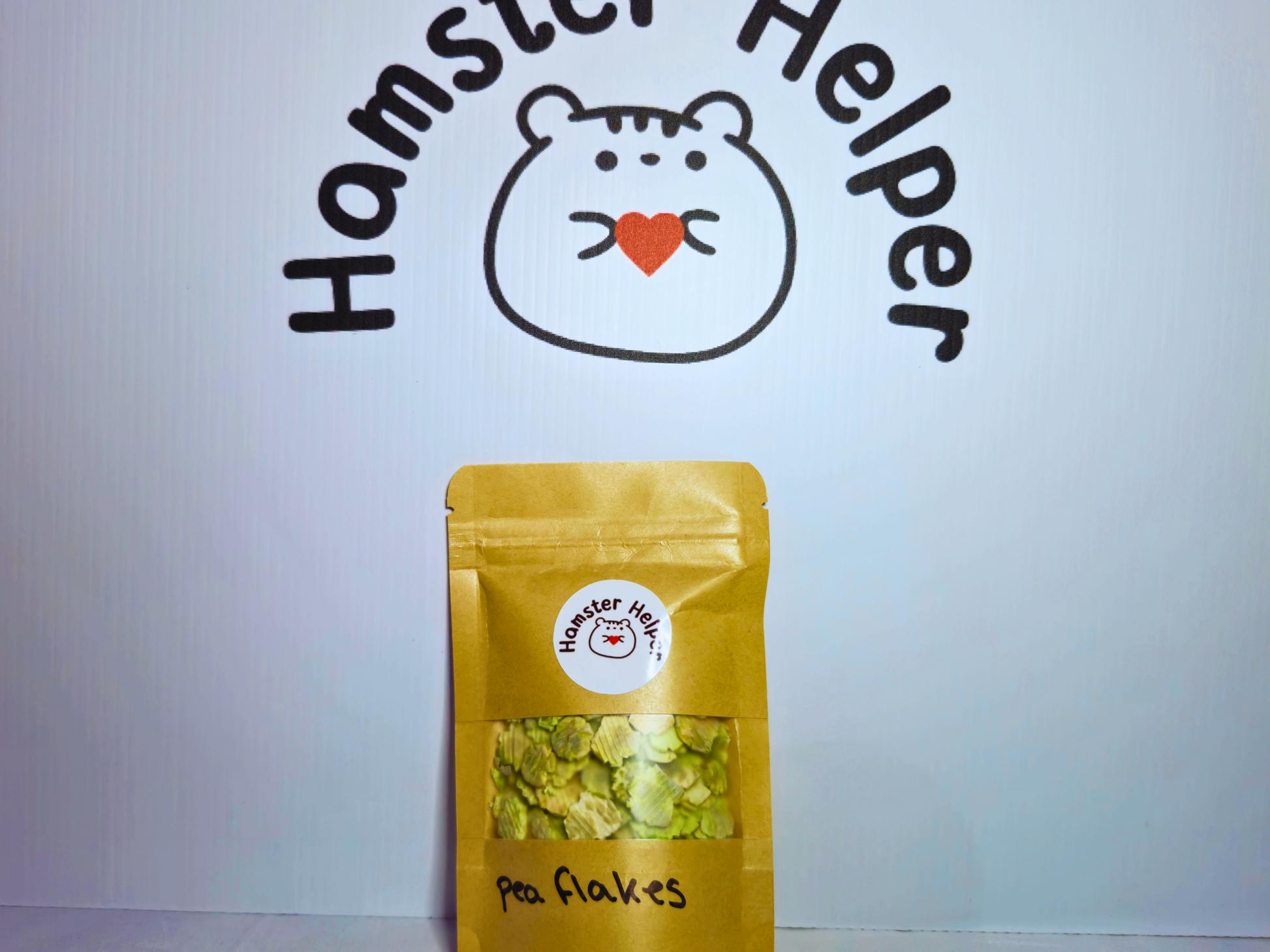 A picture of a small bag of hamster safe pea flakes in a re-sealable bag placed in front of the hamster helper logo