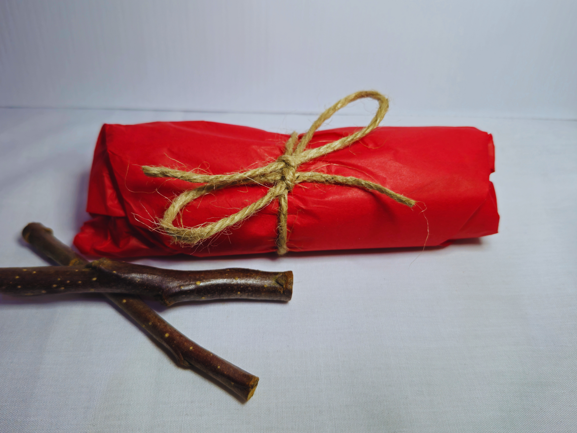 50g of Hamster safe organic apple wood chews wrapped in red tissue paper and tied with Jute twine to demonstrate packaging.