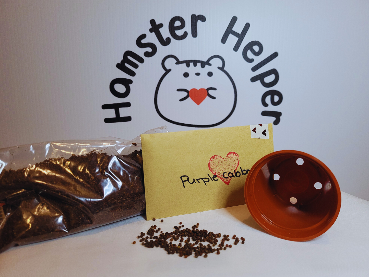 A hamster safe purple cabbage microgreen kit containing a small bag of hamster safe soil, a pack of purple cabbage microgreen seeds and a plastic pot in front of the Hamster Helper logo.