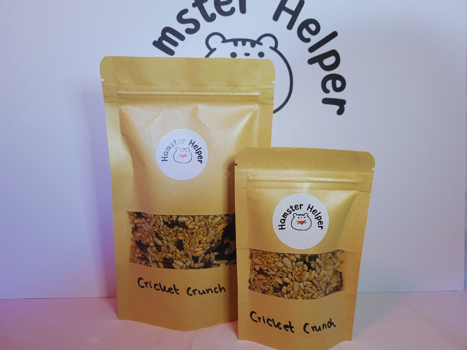 A small and large pouch of cricket crunch hamster treat mix next to each other both with the Hamster Helper logo on them.